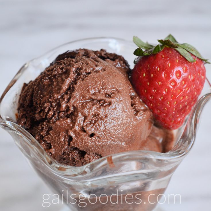 A close up view of a scoop of chocolate sorbet in a sundae glass. The dark chocolate sorbet is garnished with a single strawberry.