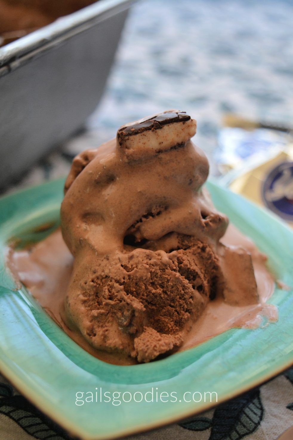 A green bowl holds two scoops of chocolate peppermint patty ice-cream. The top scoop is partly melted revealing a peppermint pattie piece on top and in the middle. The bottom scoop is solid showing a creamy chocolate ice-cream.