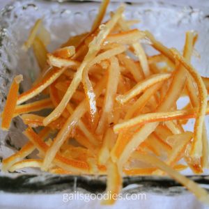 Candied Citrus peel in a hammered glass dish. The peel is cut into thin strips that are dark orange on one side and pale yellow on the other.