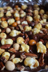 A closeup of uncut mocha caramel popcorn bark. The dark chocolate is dotted with pieces of golden caramel corn, medium and pale brown m&ms, and pecans.