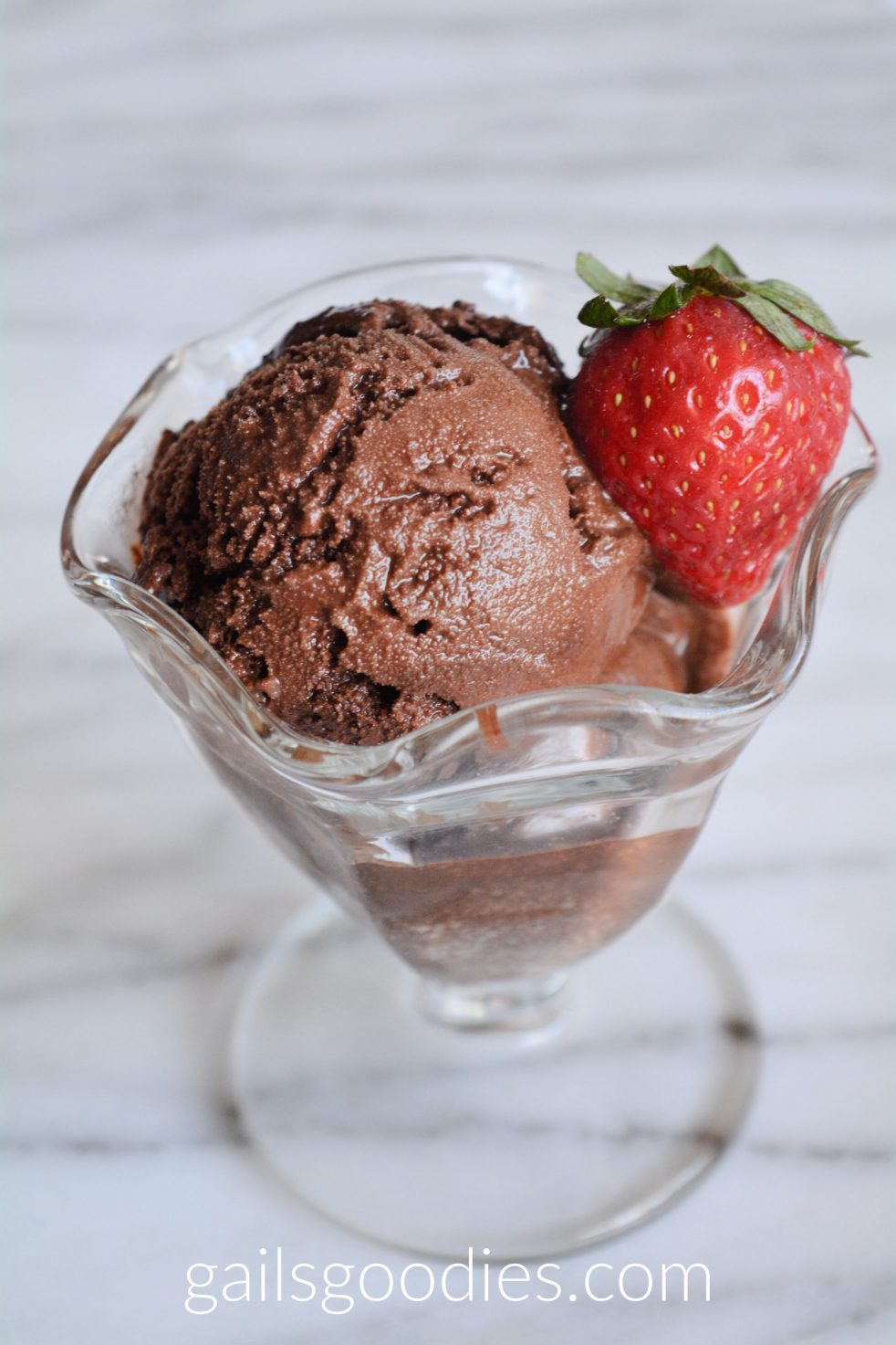 Scoops of chocolate sorbet in a sundae glass. The creamy dark chocolate sorbet is garnished with a single strawberry.