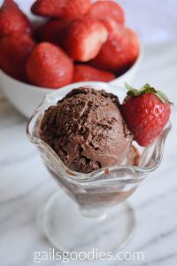 Scoops of creamy dark Chocolate sorbet in a sundae glass garnished with a single strawberry.  A bowl of fresh strawberries is in the background to the left.