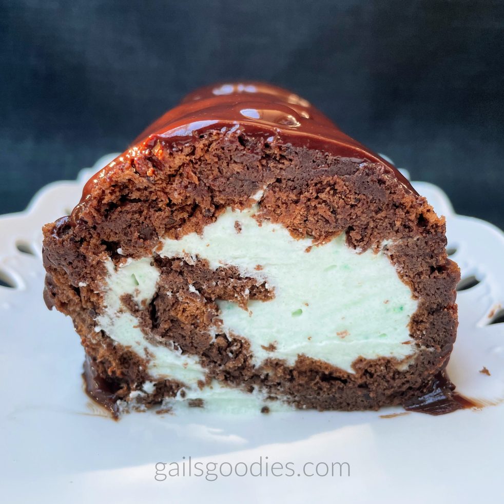 This is a view of the end of the chocolate mint cake roll. The moist chocolate sponge spirals around the light green mint whipped cream in a clockwise direction. There is a thin coating of shiny dark chocolate mint ganache surrounding the slice.