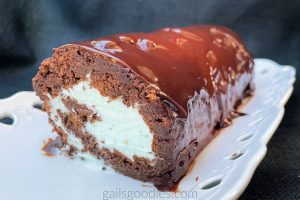 This is a view from about forty-five degrees to the side. The cut end of the cake roll shows a spiral of moist chocolate sponge cake and light green mint whipped cream. The outside of the cake roll is coated in shiny dark chocolate mint ganache.