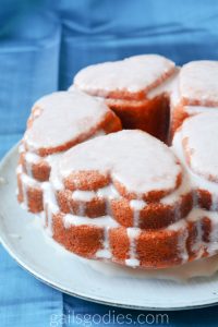 The bundt cake is five hearts. The cake is glazed with a light pink glaze that drizzles down the sides.