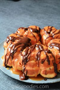 This is a view of the left side of a loaf of chocolate caramel monkey bread. The golden bread has segments that can be pulled apart. Chocolate syrup and caramel sauce a generously drizzled over the top of the ring-shaped loaf.