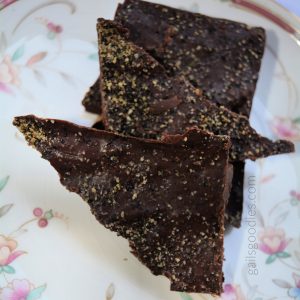 Triangular pieces of dark chocolate sprinkled with cracked black pepper are stacked vertically on a floral plate.