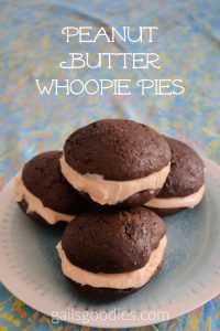 Four peanut butter whoopie pies are stacked in a pyramid on a light teal plate. Three whoopie pies are on the bottom and one is on top. Two on the bottom and one on the top. A thick layer of creamy peanut butter filling is sandwiched between two large, moist chocolate cake cookies.