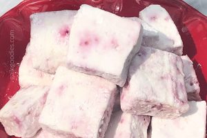 A close up shot of a pile of peppermint stick marshmallows on a red plate. The square marshmallows are slightly pink with darker pink spots.