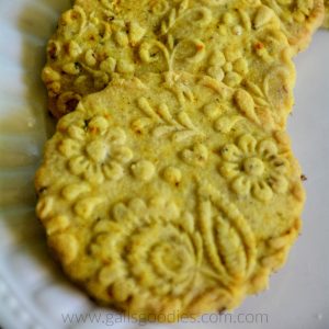 This shot is a closeup of Turmeric shortbread cookies. The golden yellow round cookies are embossed with flowers and have scallopped edges. Small orange flecks of turmeric tea dot the cookies.